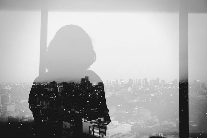 double exposure of woman looking out onto city from tall building