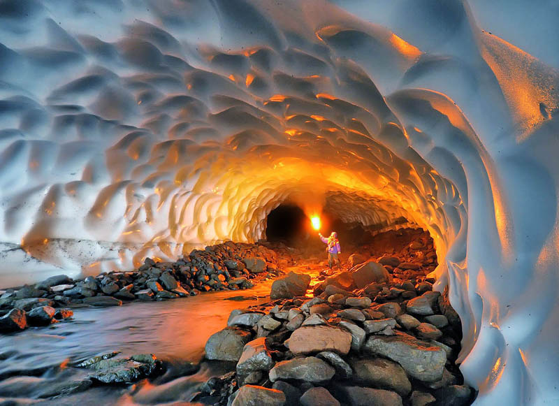 picture at the start of a 1km long snow tunnel with person facing camera lighting up the tunnel with a fire torch