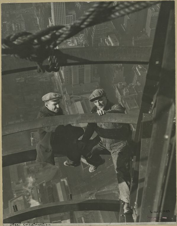 Two workers inspecting steel high up no harness city in backdrop