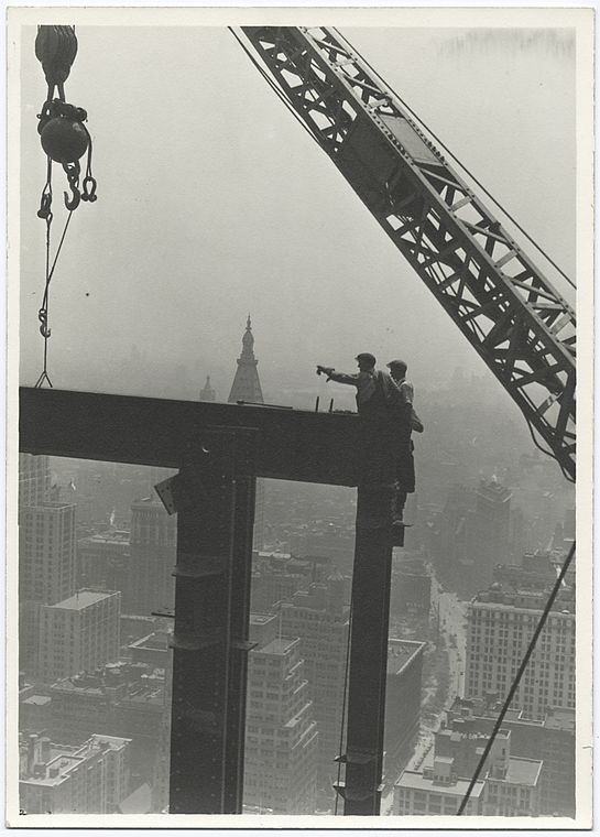 Two construction workers at the corner of two steel beams pointing to the left (1931)
