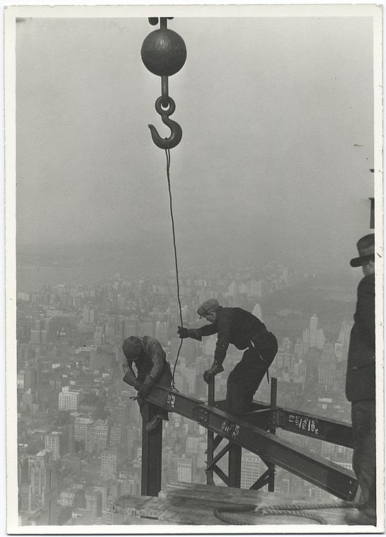 two workers attaching beam with a crane high up empire state building 1931 no safety harnesses