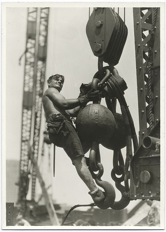 a worker riding on a massive crane hook