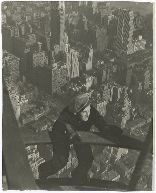 a worker hanging on two steel beams very high up with city of new york in background