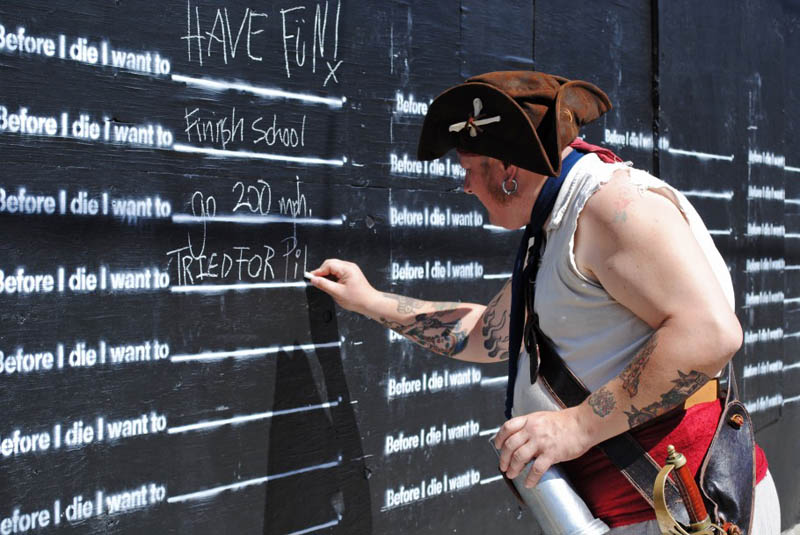 man in pirate hat writing on before i die wall