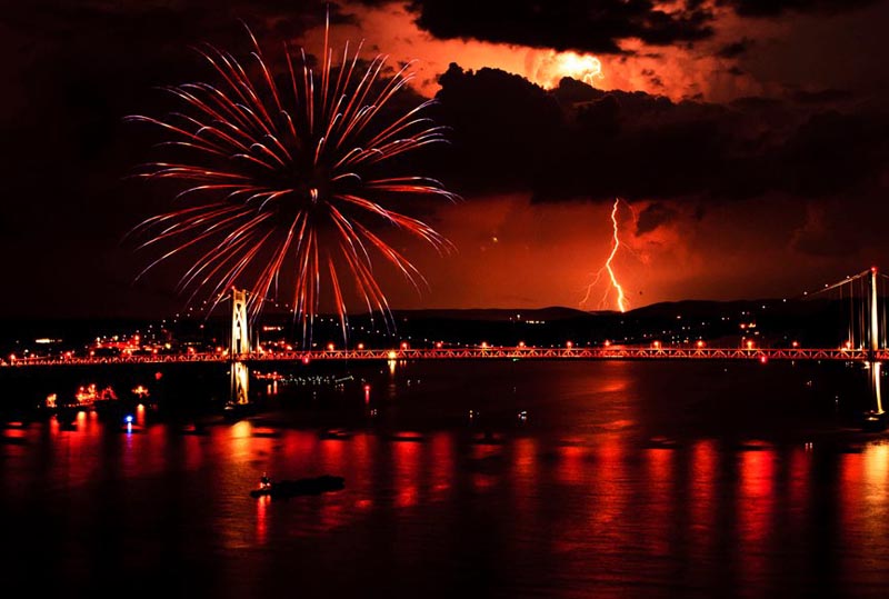 a bolt of lightning lights up the sky at the exact same moment as a large fireworks display