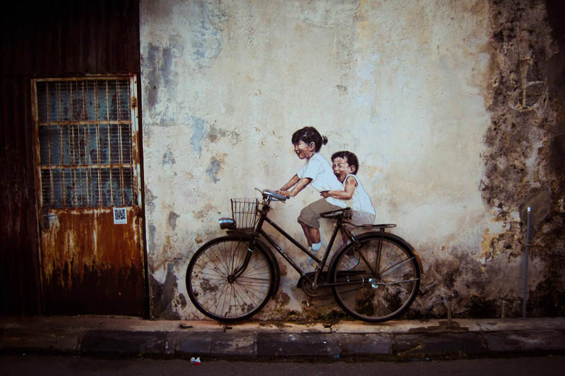 artwork of girl and boy on a wall with a real bicycle placed in front that looks like they are riding it