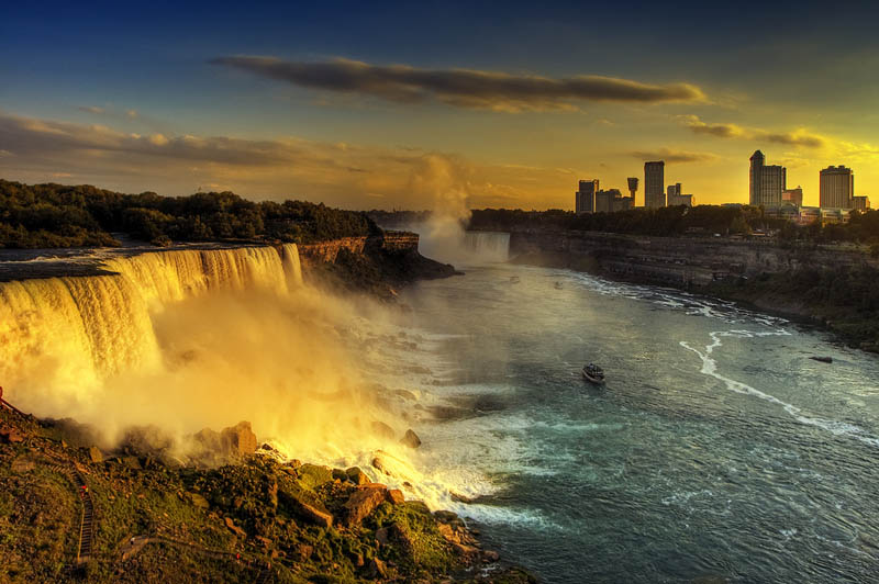 wide angle view of niagara falls with maid of the mist ship visible in the shot golden rays of sunshine on falls