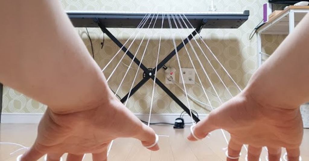 Watch This Musician Play Piano From Their Bed Using Finger Strings