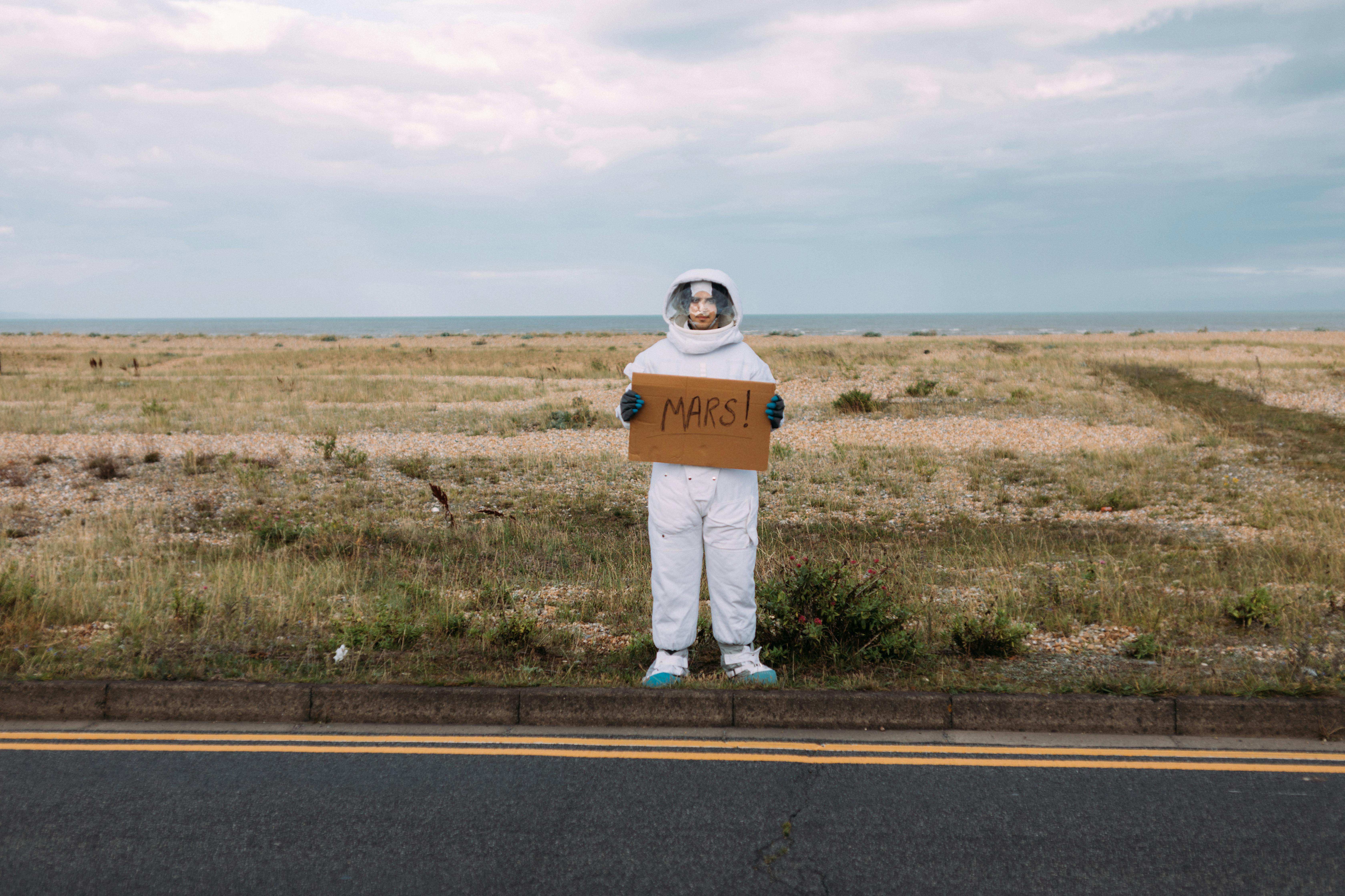 Astronaut holding a sign that says Mars on the side of the road