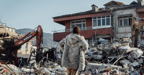 A woman surveying earthquake damage beside a digger