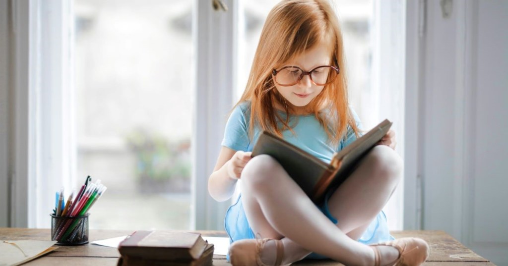 A red-haired girl reading in a window