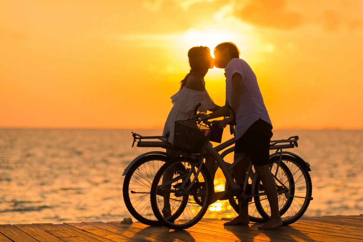 A couple with bicycles sharing a sunset beach kiss