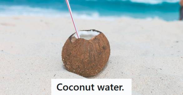 A coconut drink with a straw sitting on the beach
