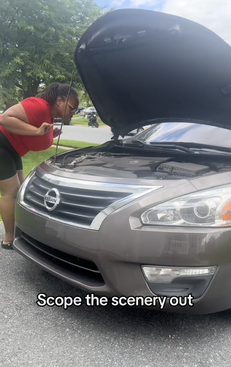 woman looking under the hood of a car