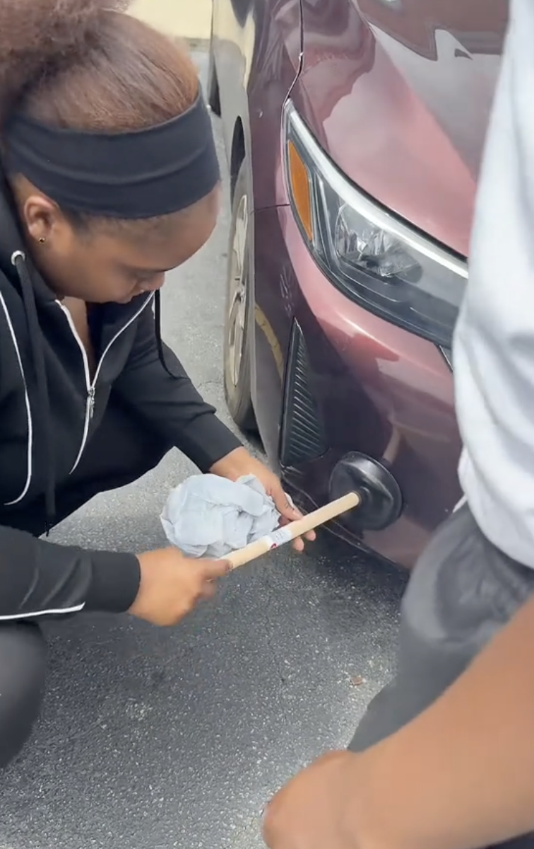 woman using a toilet plunger on a car