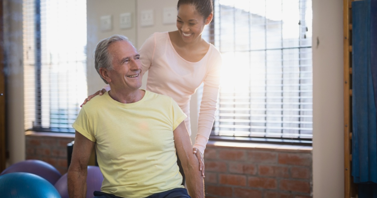 Older man sitting with nurse helping