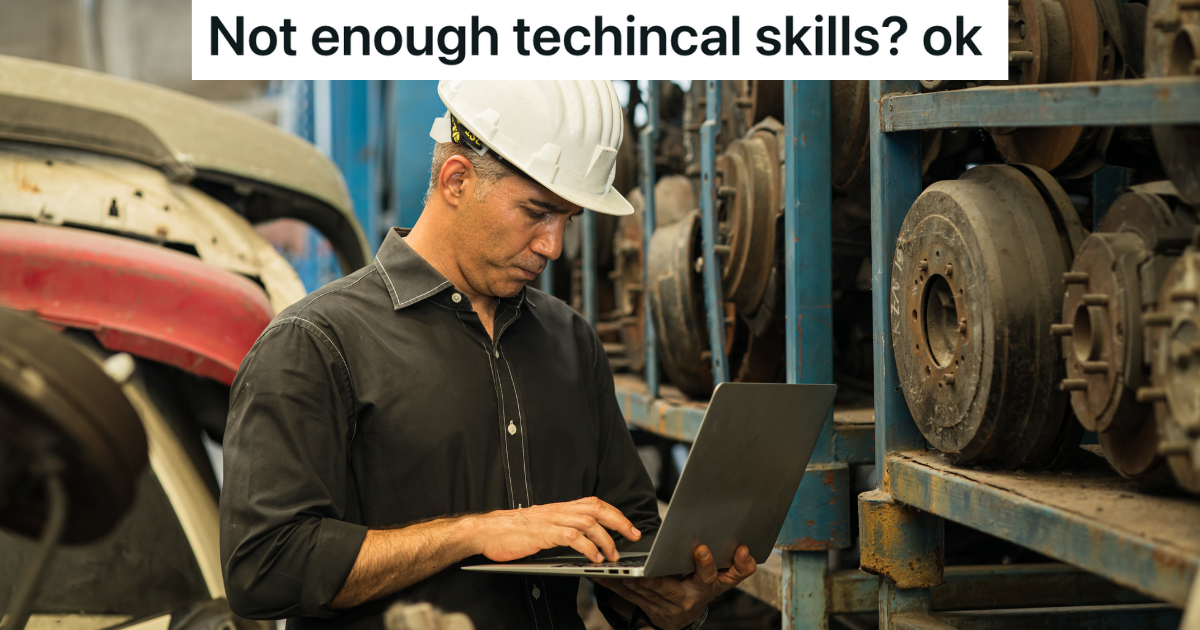 man in a junkyard wearing a hardhat and looking at a laptop