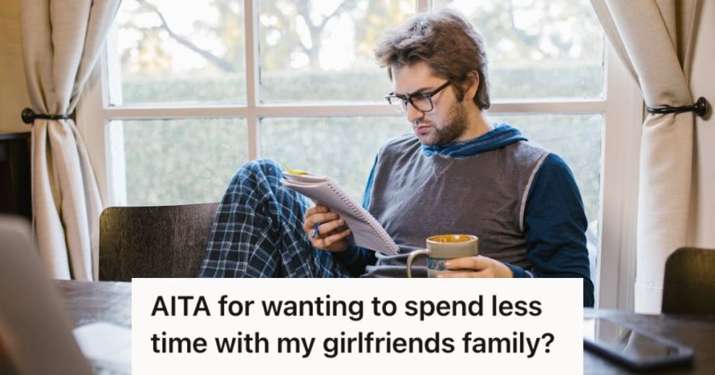 Man reading a notebook and holding a cup of coffee while sitting near a window