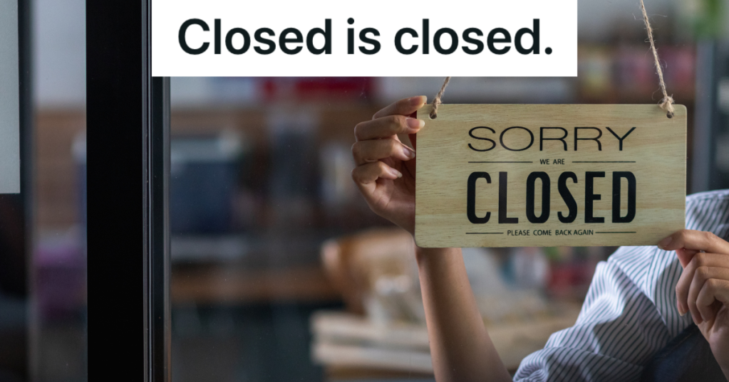 closeup of employee's hands putting sign in store window that reads "sorry closed"