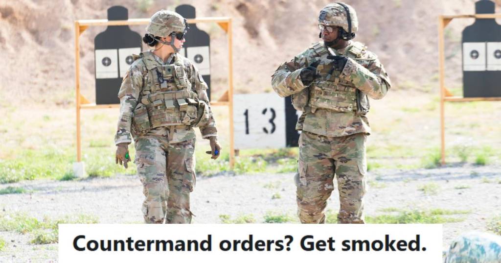 Two military members walking in full gear down a gravel road