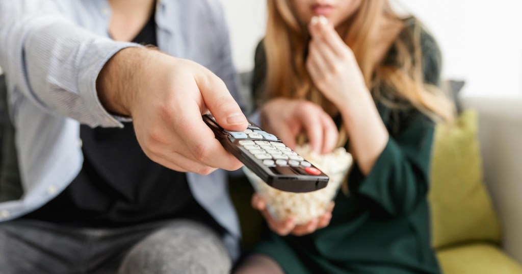 A couple with popcorn pressing a TV remote
