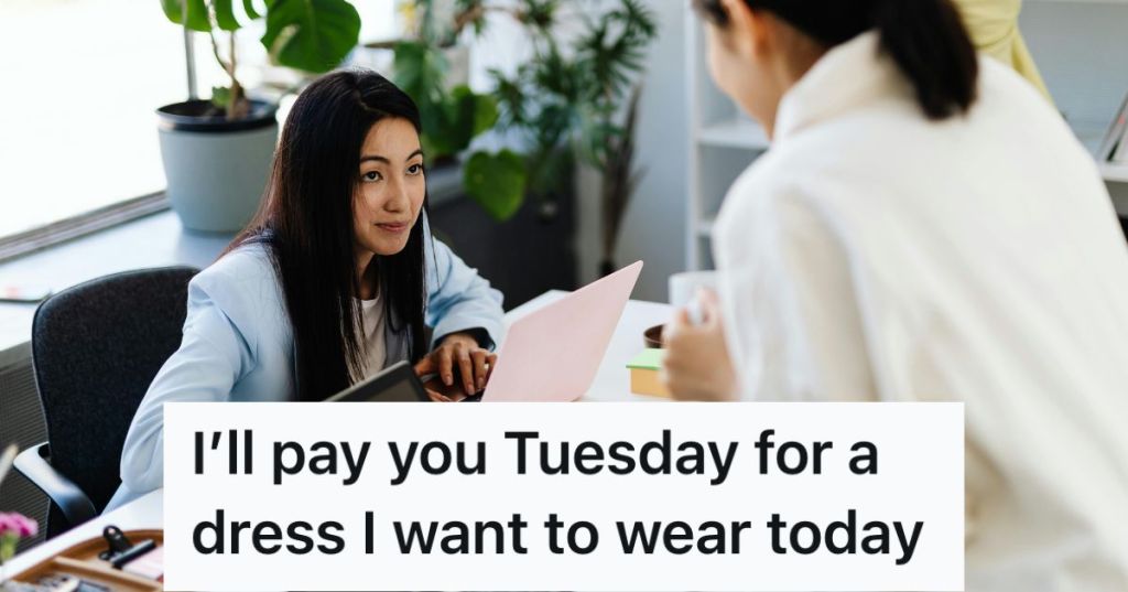 Woman on a laptop looking up to another woman standing in front of her in an office