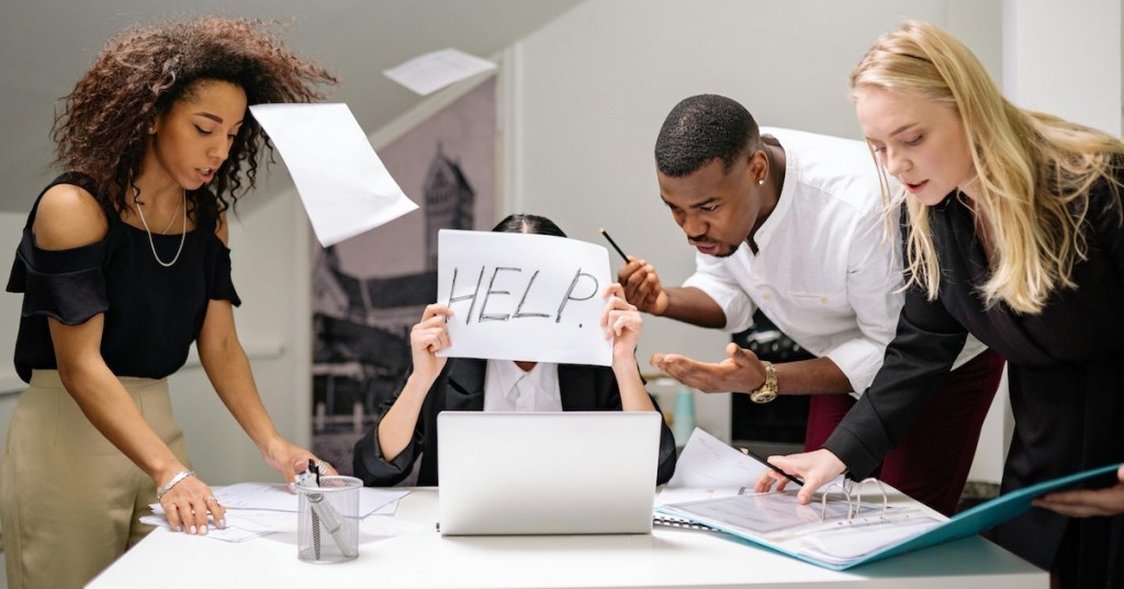 A woman surrounded by colleagues holding a 'help' sign