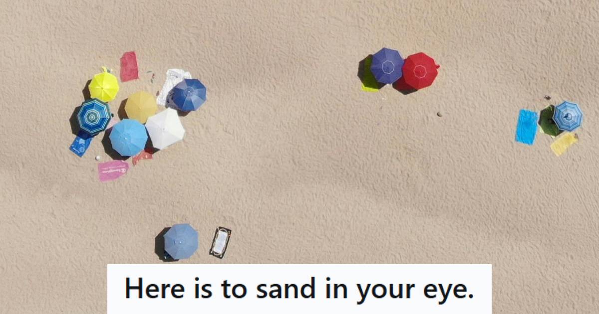 Beachgoers set up on the beach under umbrellas on a sunny, clear day