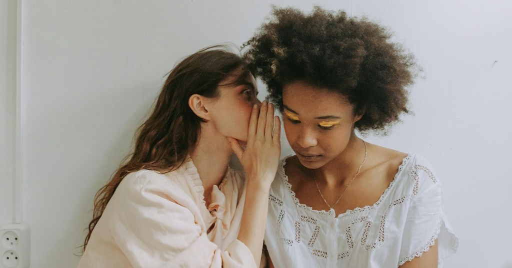 A woman whispering into another woman's ear