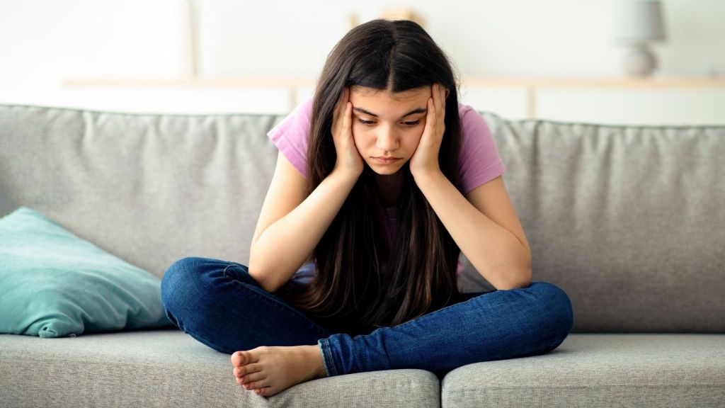 sad teenage girl sitting on the couch looking down