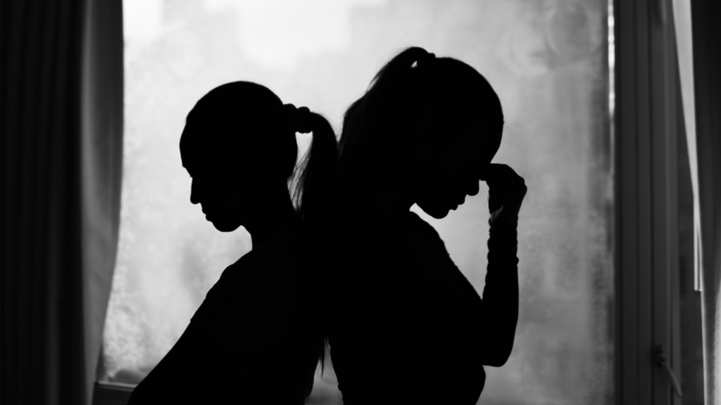 Two women stand back to back in a sad looking silhouette