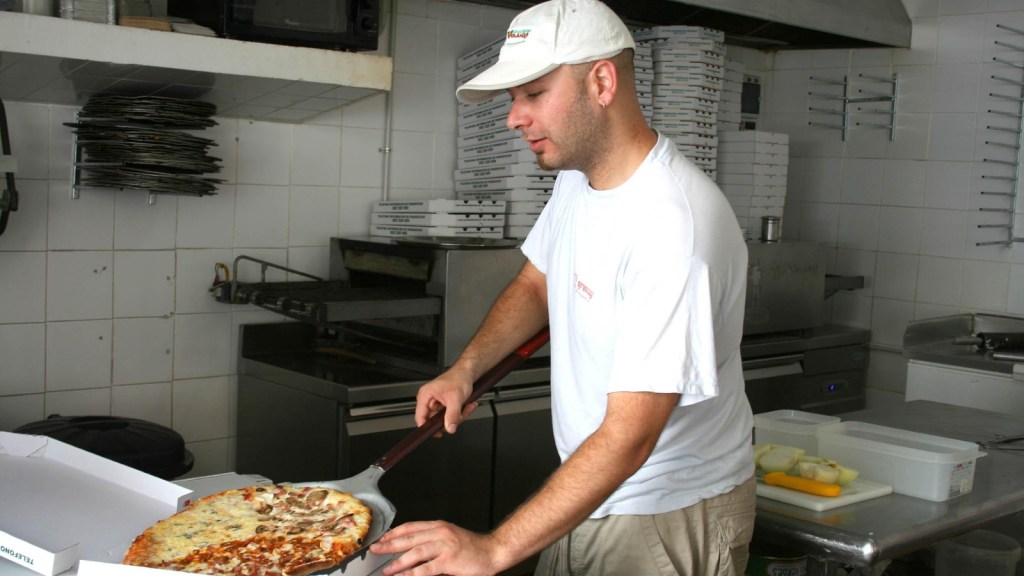 An employee making a pizza at a restaurant