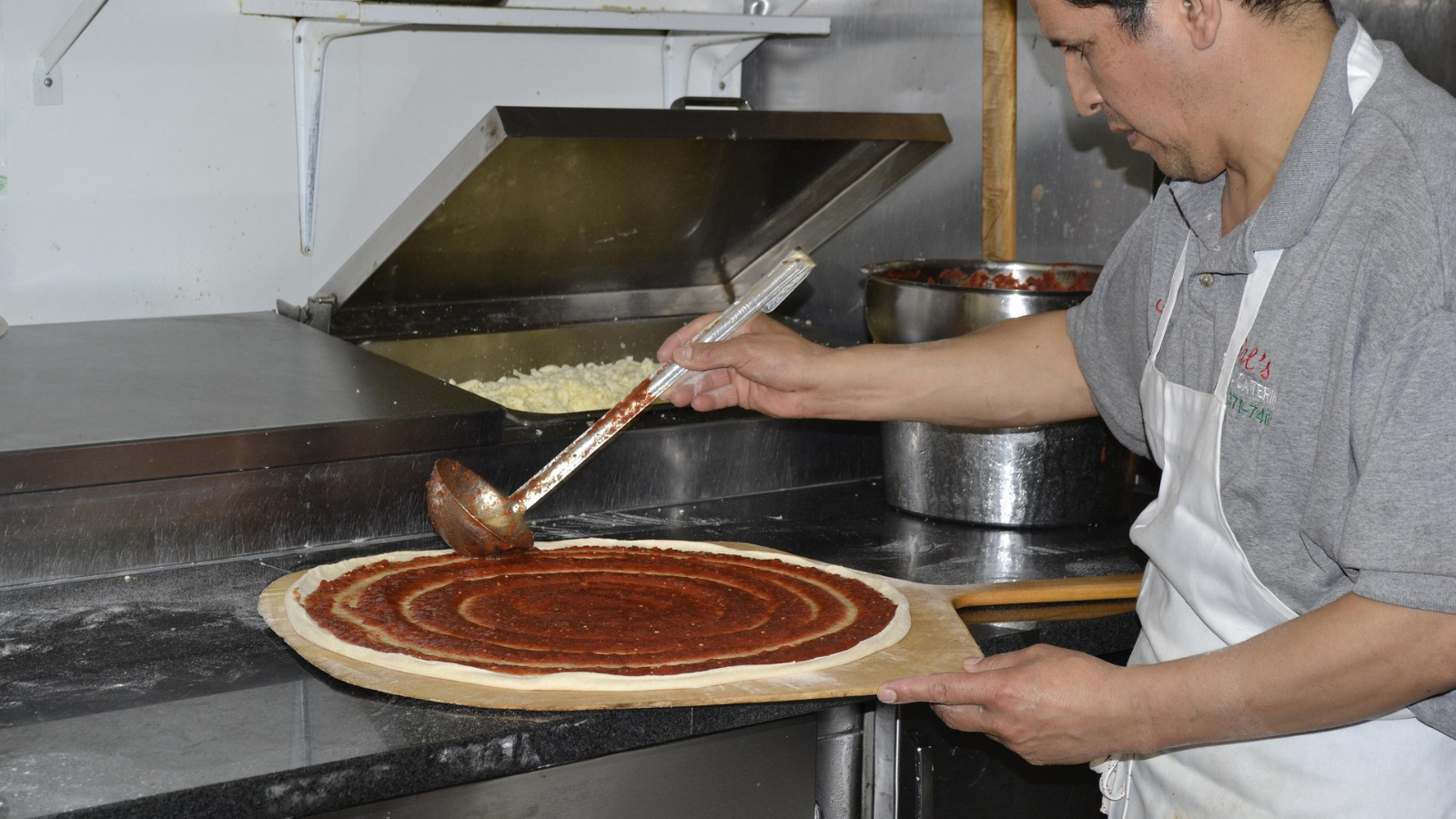 A man saucing a pizza in a restaurant