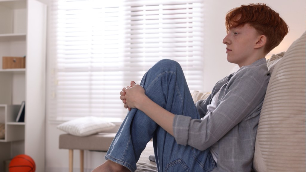 A teenage boy looking upset, sitting on a couch