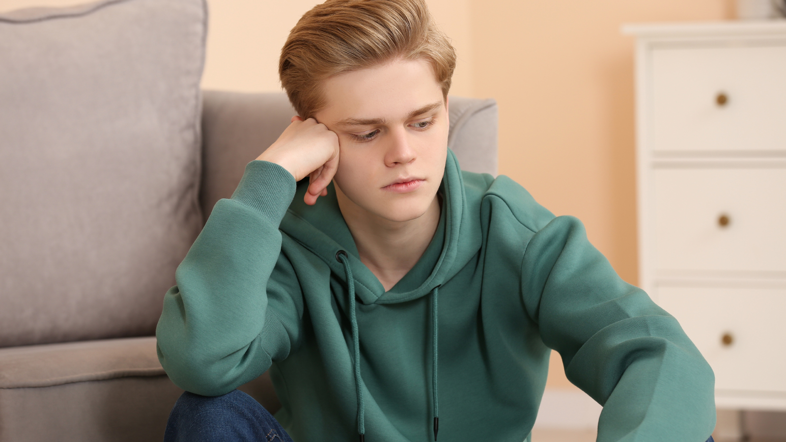 A young man sitting on the floor looking upset