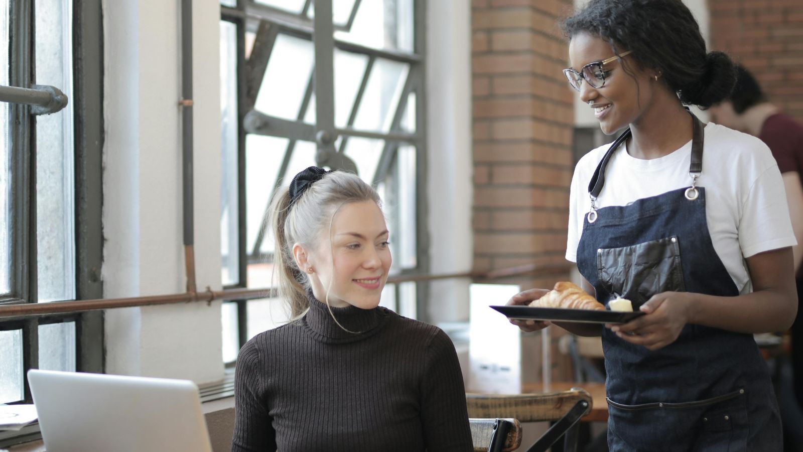 Woman serving food to a customer on her laptop
