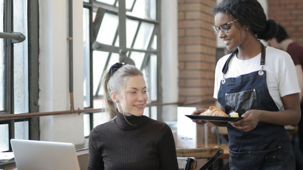 Woman serving food to a customer on her laptop