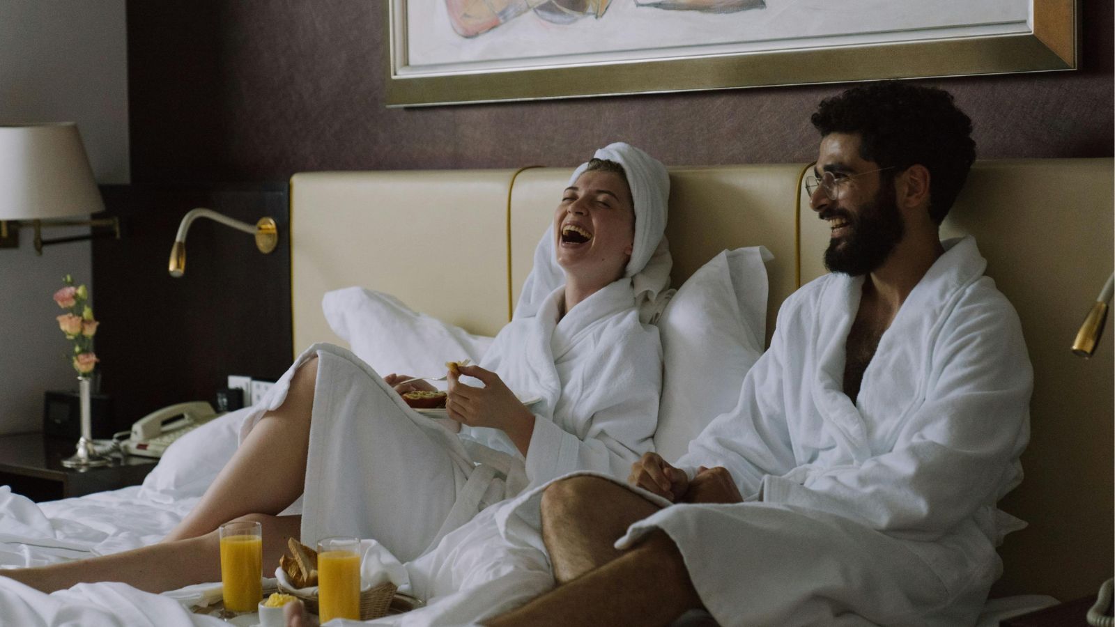 Couple sitting on hotel bed laughing