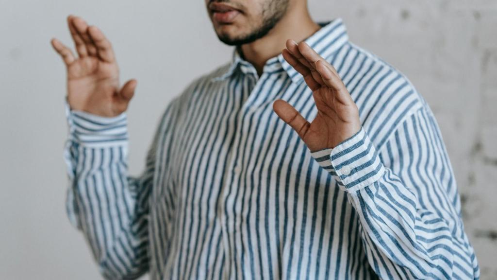 Man in blue and white striped shirt holding his hands up