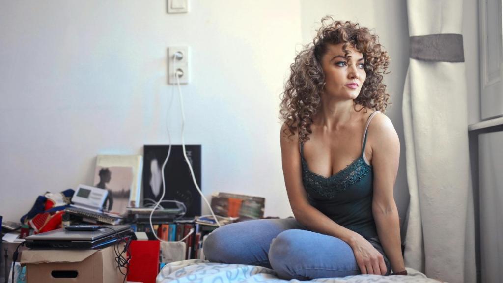 Woman sitting on her dorm room bed, looking out the window