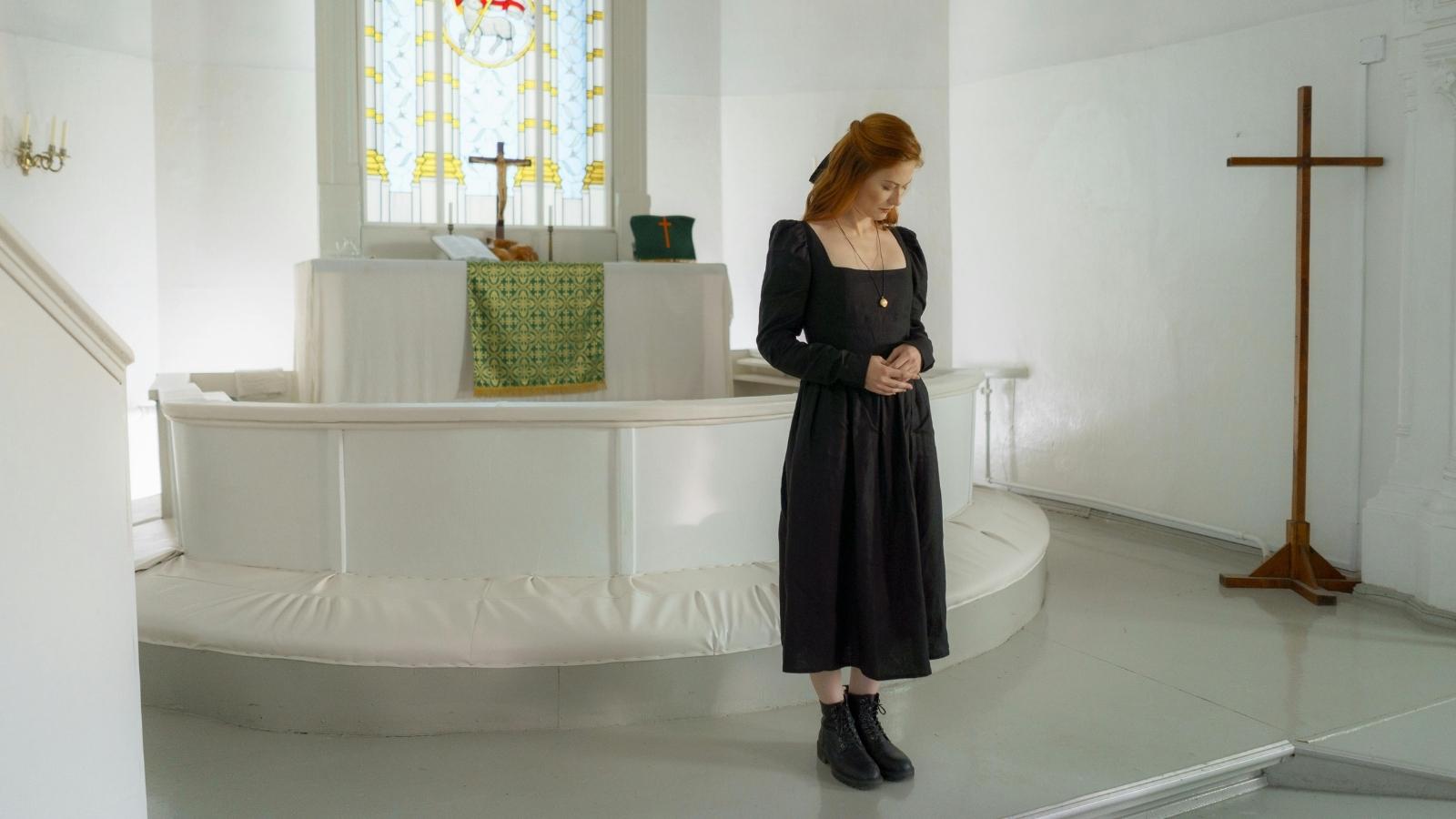 Woman standing in a church, wearing an ugly black dress