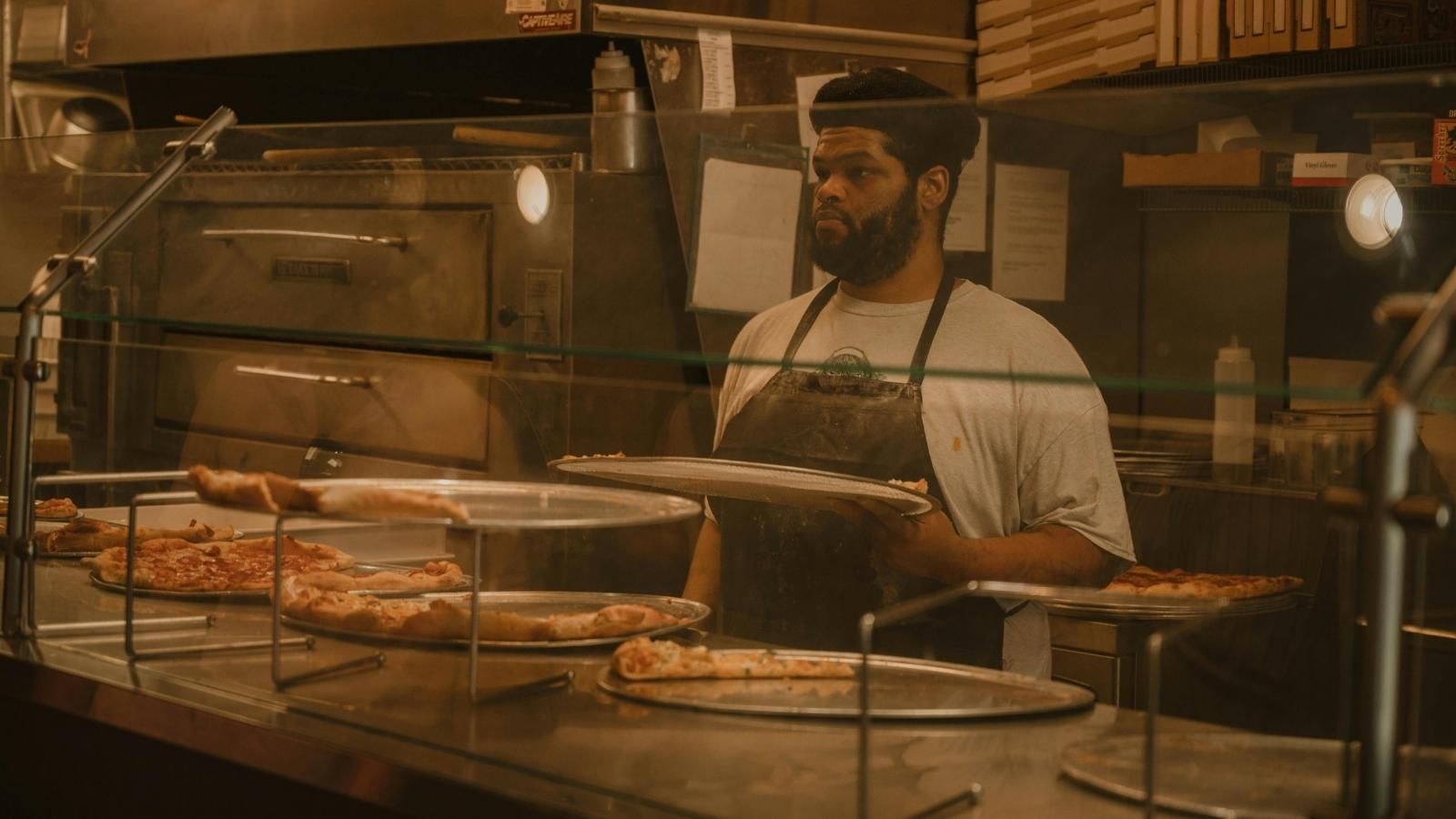 Man standing behind a counter baking pizzas