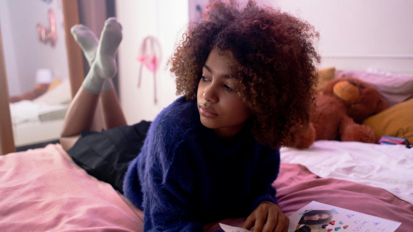 Mixed teen girl laying on her bed and thinking about work