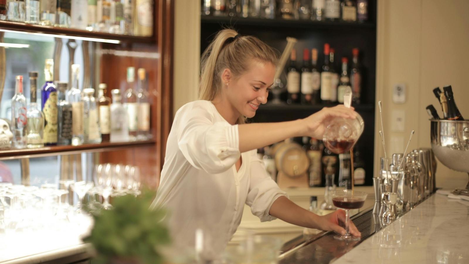 Young woman bartender pouring wine at a wine bar