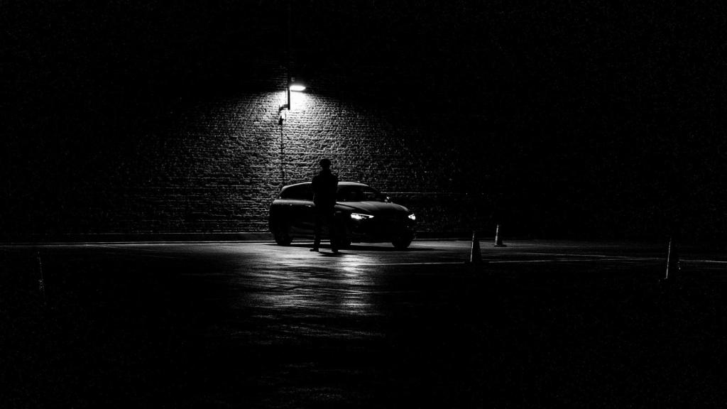 Man standing next to his car in the dark in an empty parking lot