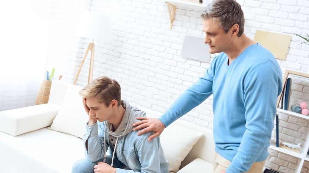 dad touching sad teenage son's shoulder