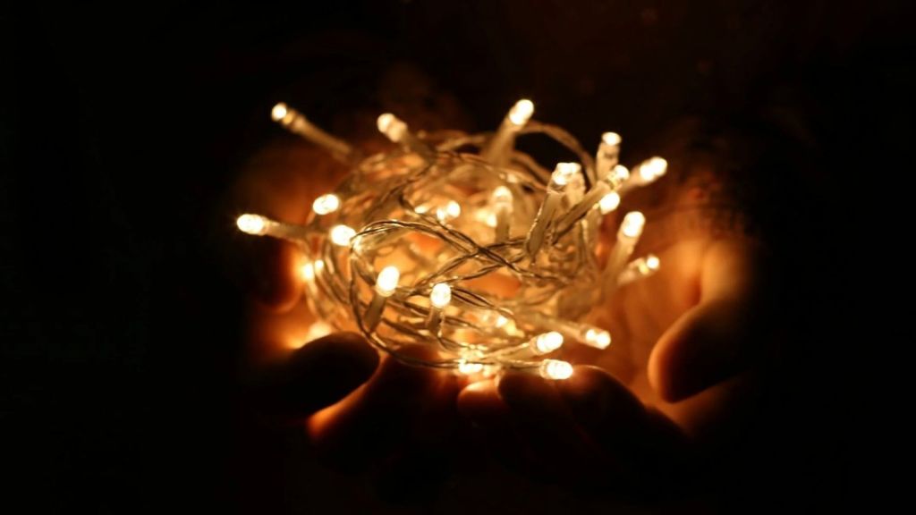 man holding illuminated string lights in the dark
