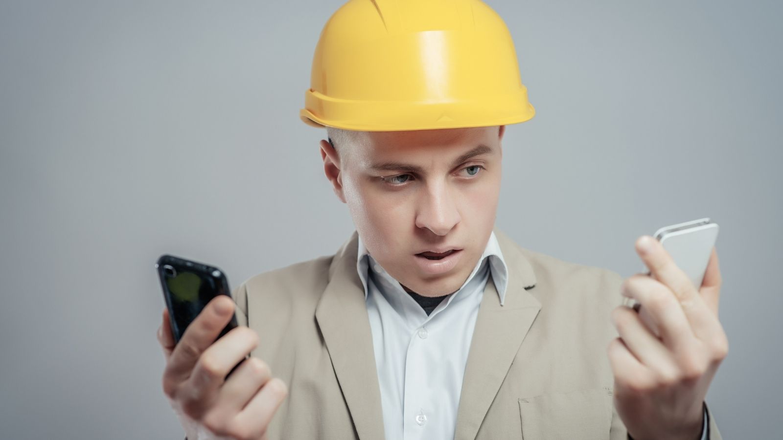upset man in a yellow hardhat holding two phones