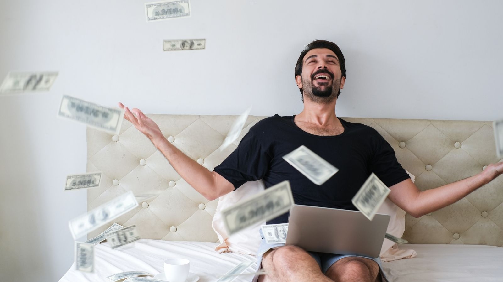 man sitting in bed throwing money in the air