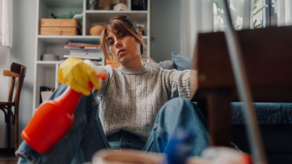 exhausted young woman holding cleaning supplies